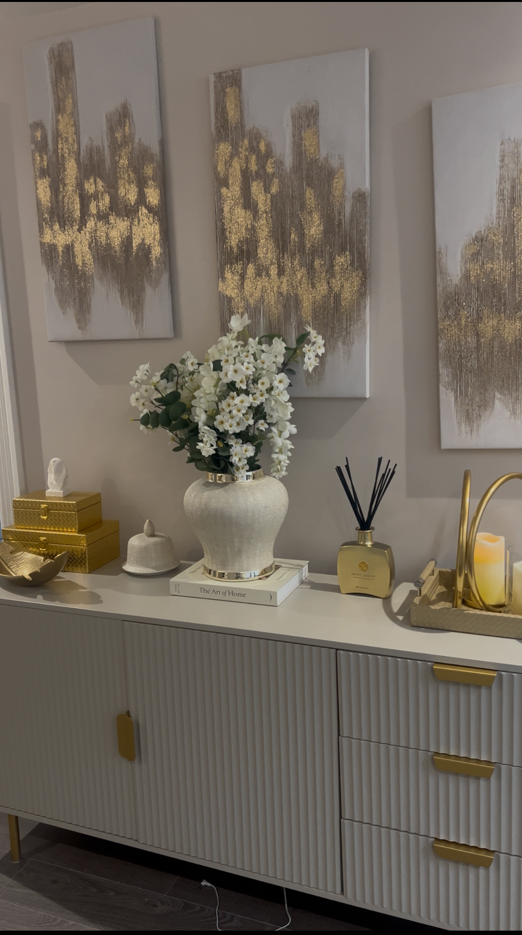 Cream console styled with gold accents, white florals and abstract canvases