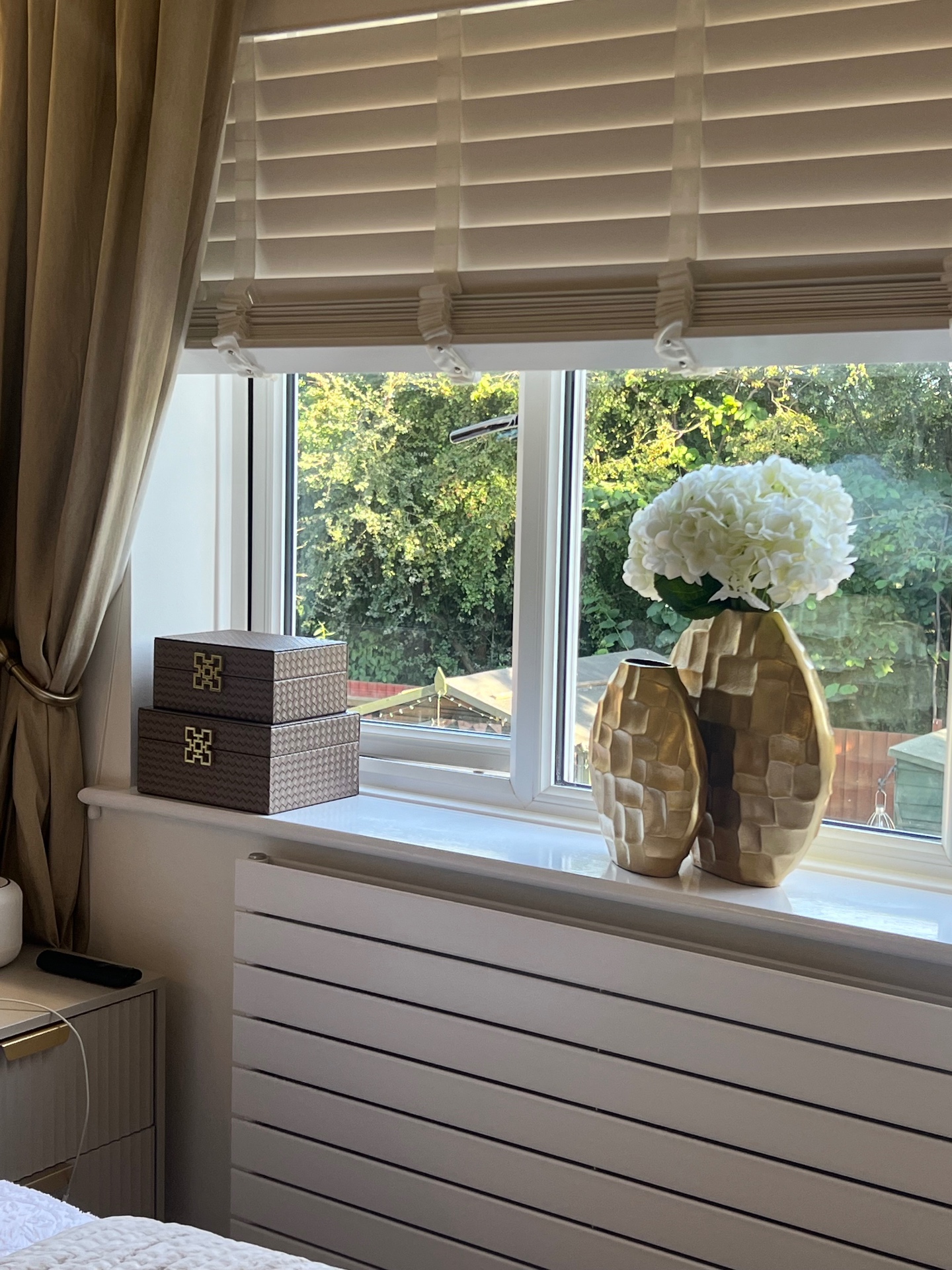 Bedroom window styled with hammered gold vases, hydrangeas and woven boxes