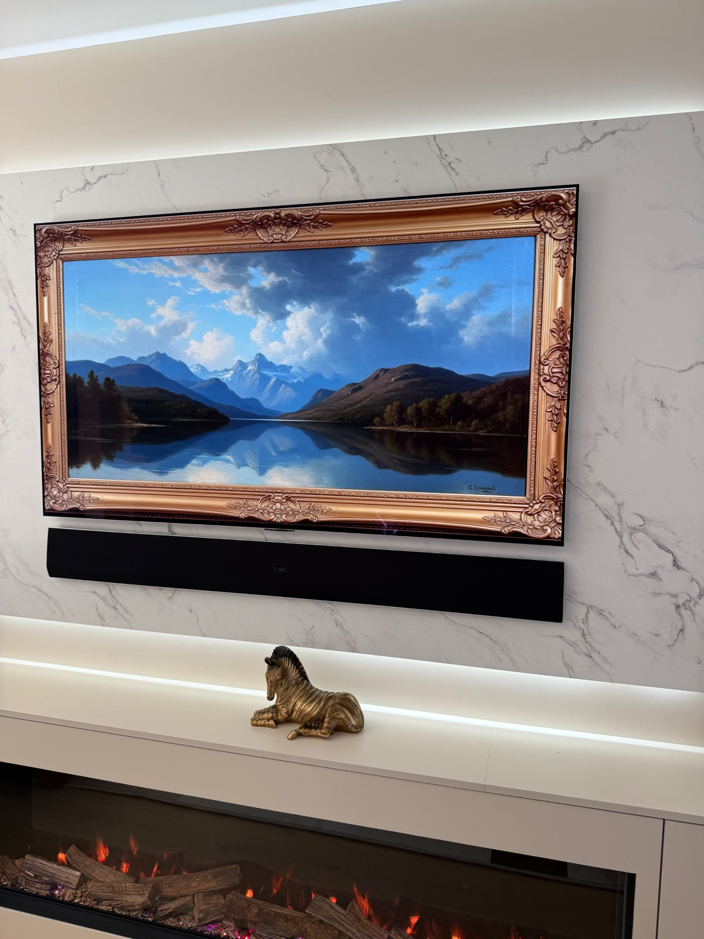 Gilt-framed art TV on marble feature wall above the fireplace