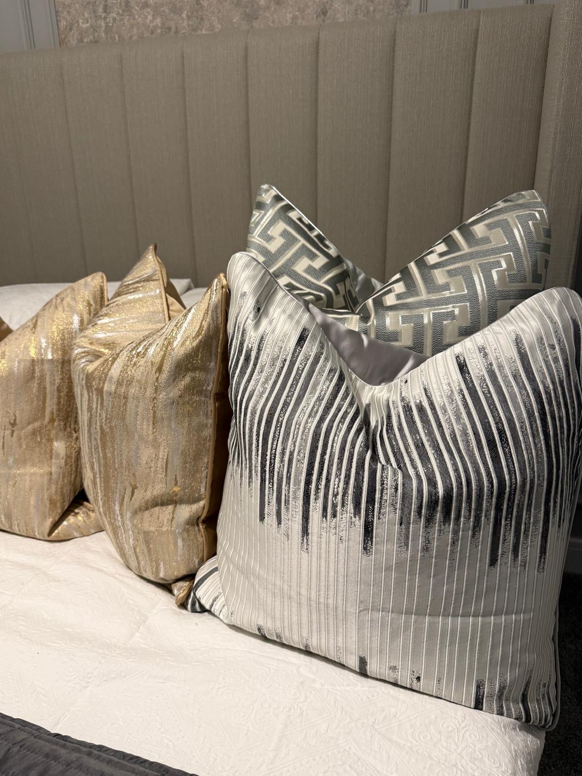 Close study of gold and silver bedroom cushions against a linen headboard